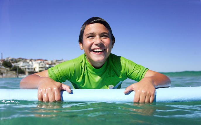 Child enjoying surf lesson at Bondi Beach, holding a surfboard in the water.