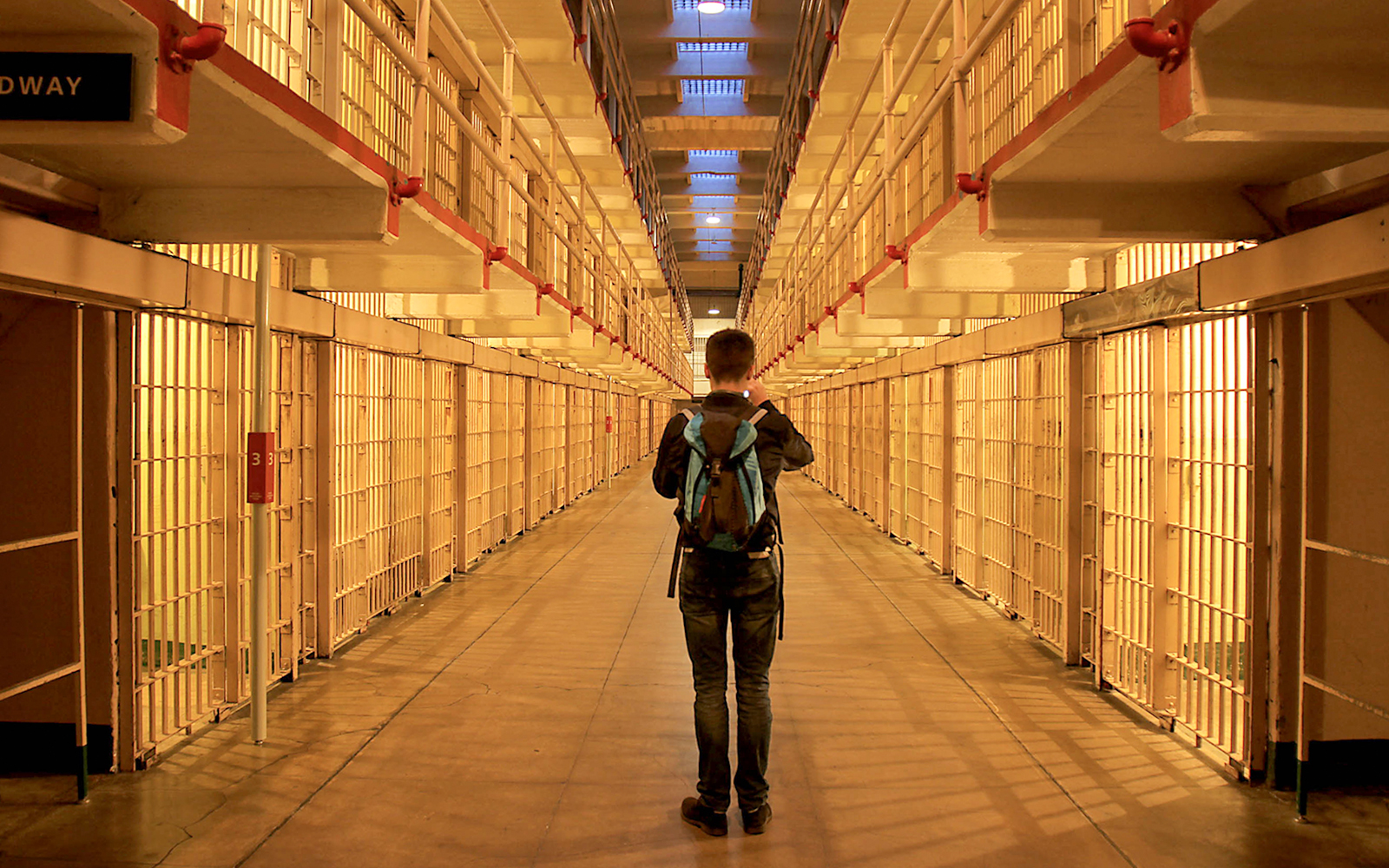 Visitor exploring Alcatraz prison cell block at night.