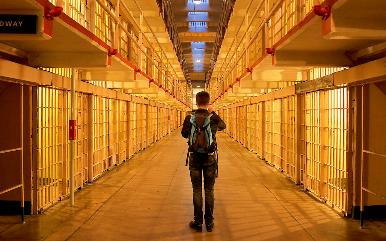 Visitor exploring Alcatraz prison cell block at night.