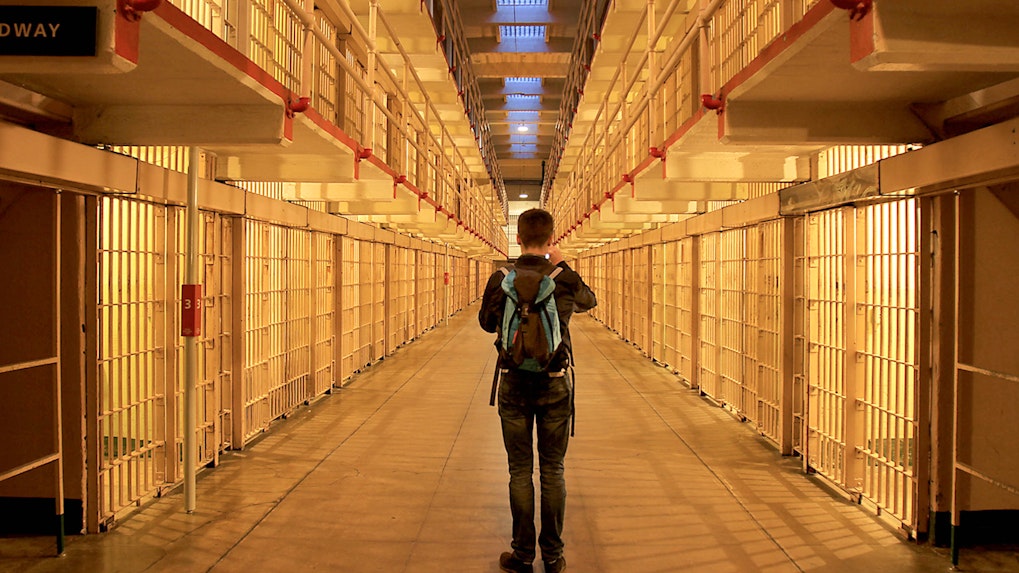 Visitor exploring Alcatraz prison cell block at night.
