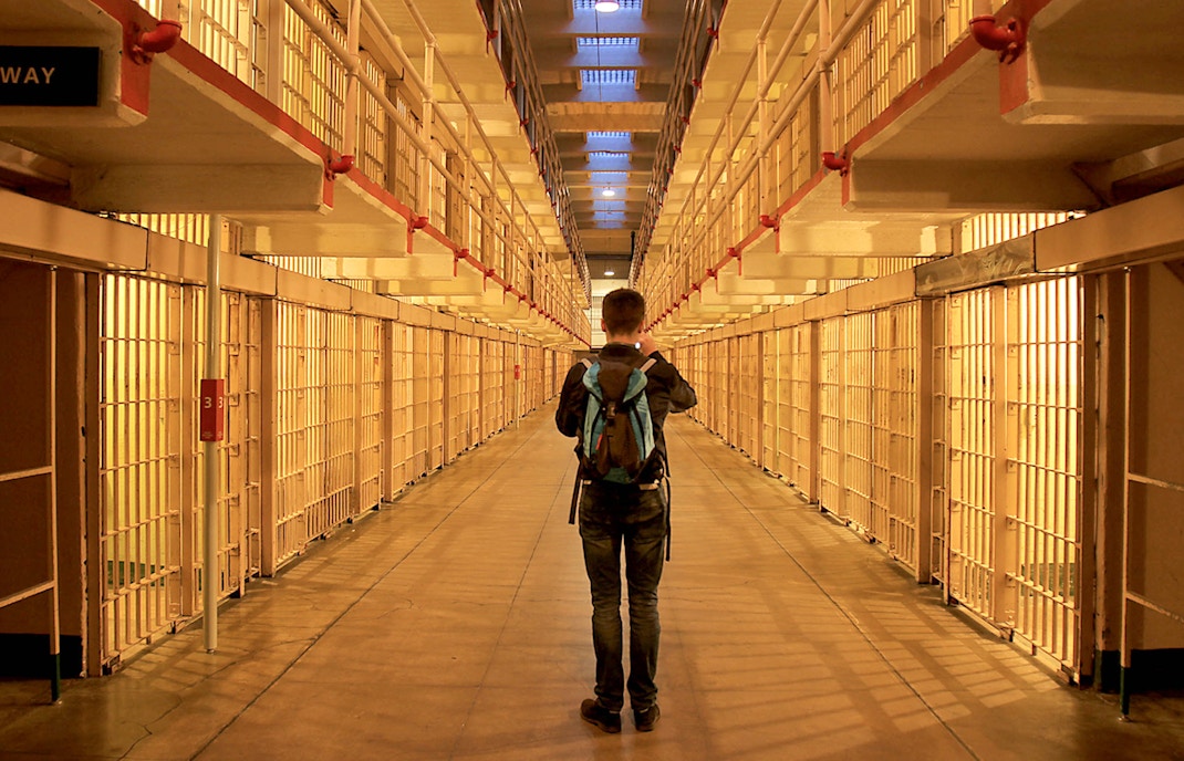 Visitor exploring Alcatraz prison cell block at night.