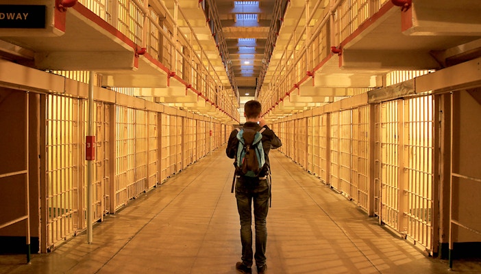 Visitor exploring Alcatraz prison cell block at night.