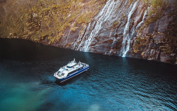 Cruise boat on Mostraumen Fjord near cascading waterfalls.