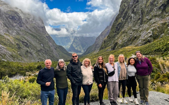 Group of tourists at Milford Sound with mountain backdrop, Te Anau departure.