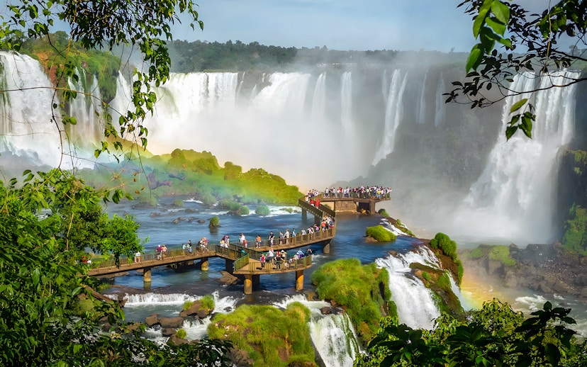 Tourists on viewing platform at Iguazú Falls, Brazilian side, with waterfalls in background.