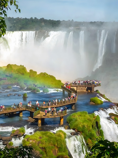Tourists on viewing platform at Iguazú Falls, Brazilian side, with waterfalls in background.