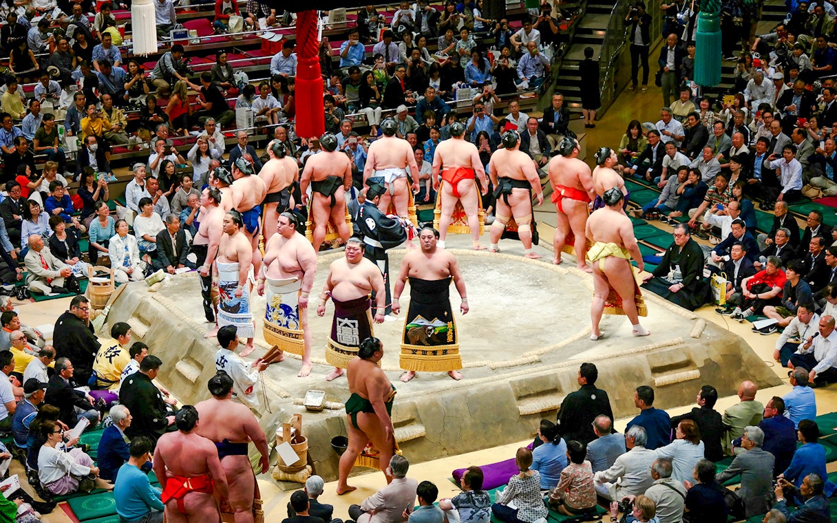 Sumo wrestlers in a Tokyo arena preparing for a match, surrounded by spectators.
