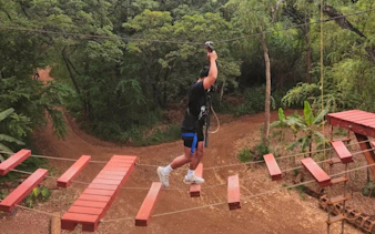 Person navigating rope bridge on adventure course in forest setting.
