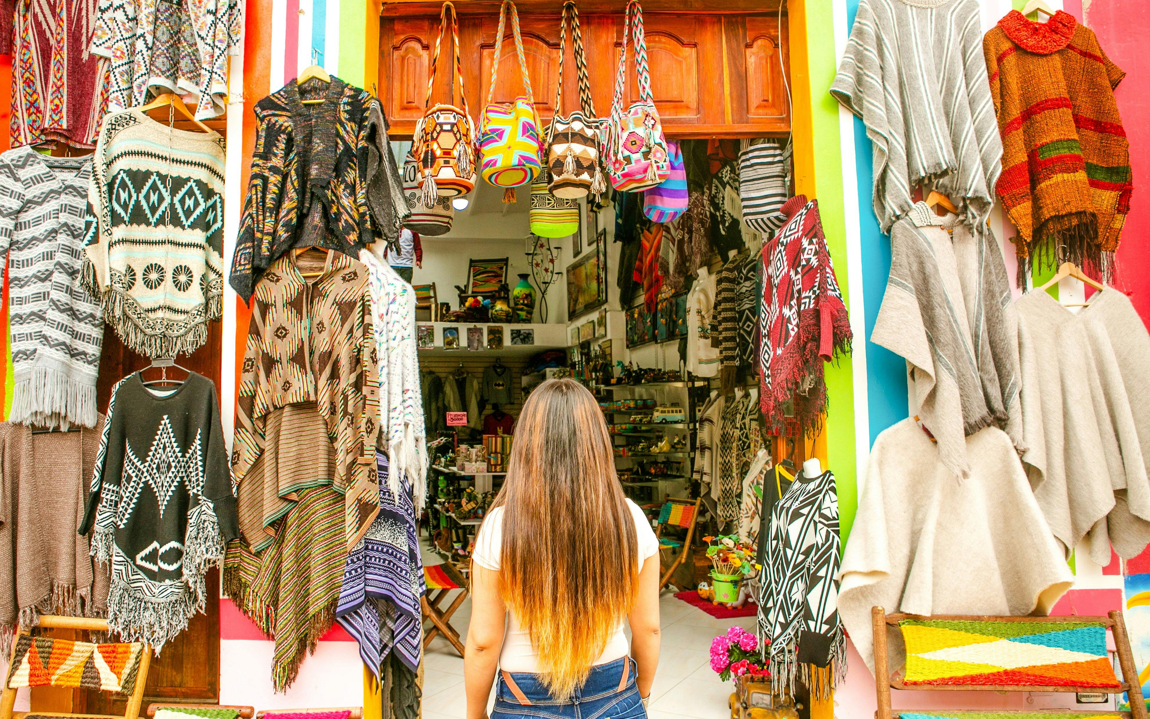 Woman shopping for colorful ponchos and bags in a Colombian market.