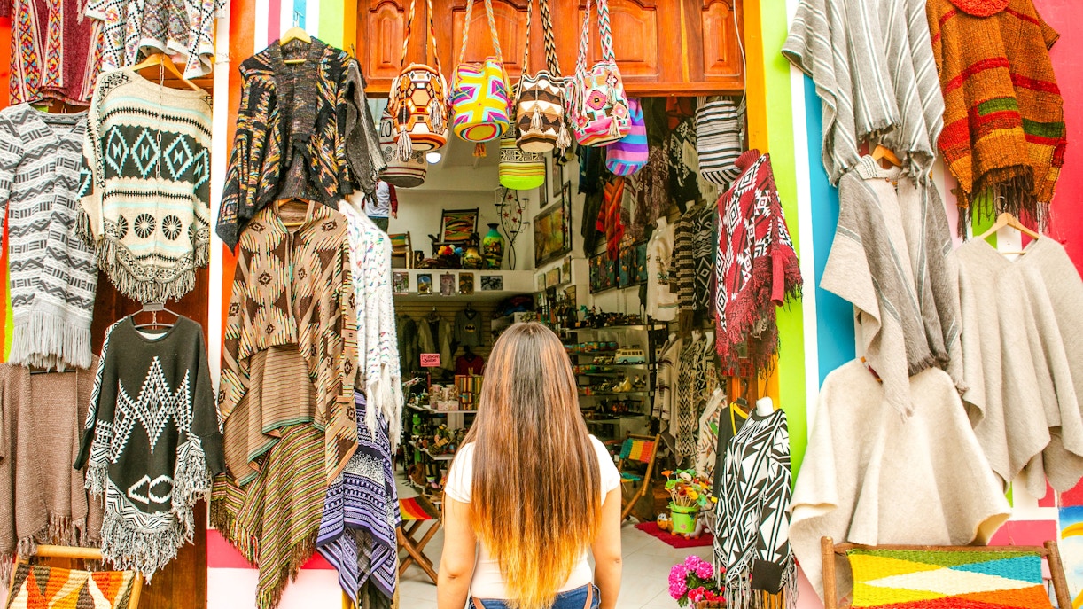 Woman shopping for colorful ponchos and bags in a Colombian market.