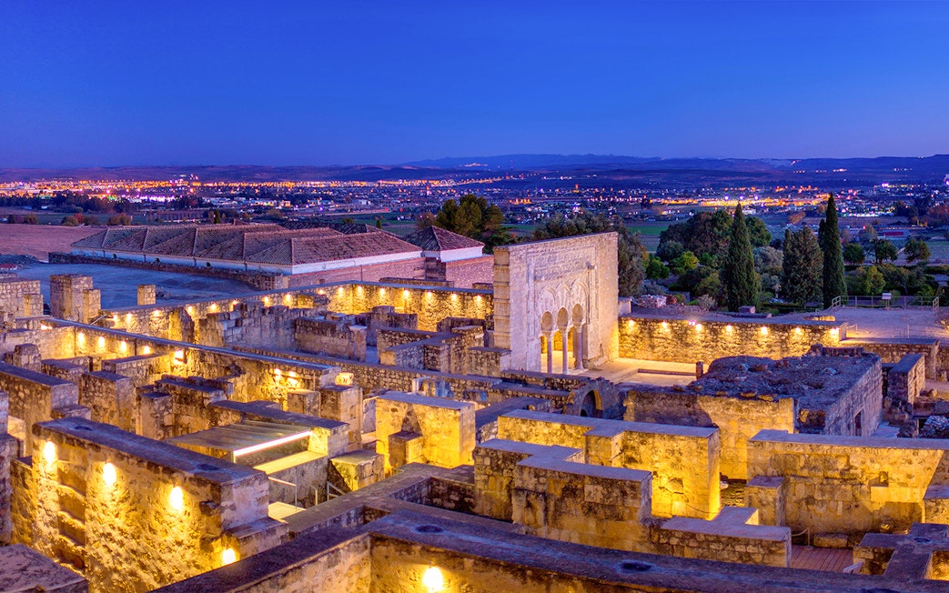 Illuminated ruins of Medina Azahara with archways and columns at dusk, Córdoba, Spain.