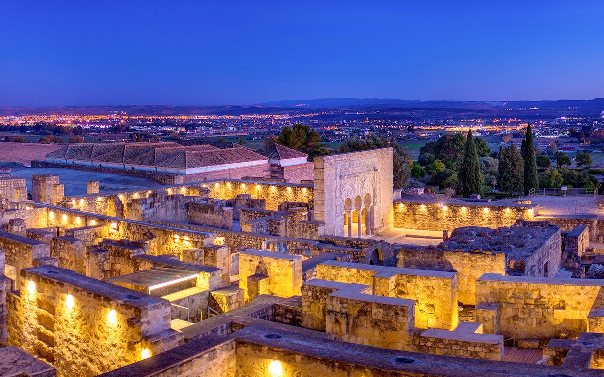 Illuminated ruins of Medina Azahara with archways and columns at dusk, Córdoba, Spain.
