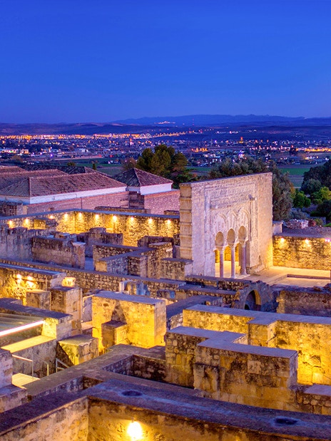Illuminated ruins of Medina Azahara with archways and columns at dusk, Córdoba, Spain.