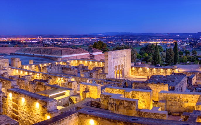 Illuminated ruins of Medina Azahara with archways and columns at dusk, Córdoba, Spain.
