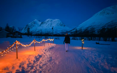 Pathway with lights in snowy Tromso landscape, mountains in background.