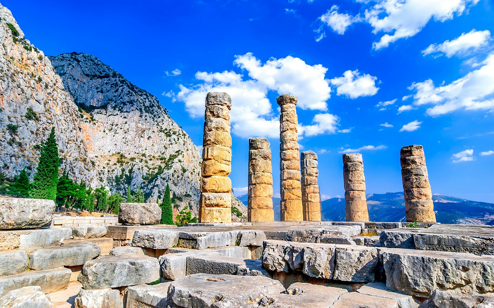 Temple of Apollo columns at Delphi Archaeological Site, Greece, with mountain backdrop.