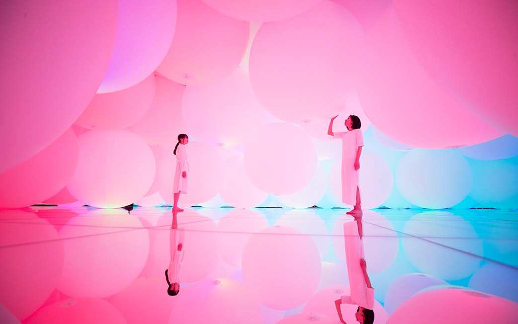 Visitors in a pink-lit room with large spheres at teamLab SuperNature Macau.