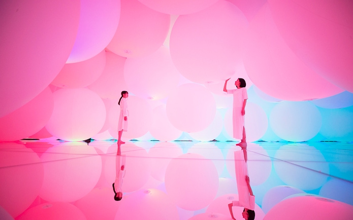 Visitors in a pink-lit room with large spheres at teamLab SuperNature Macau.