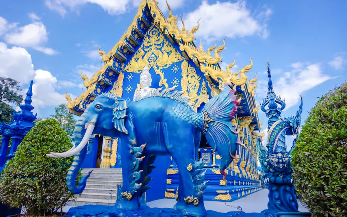 Blue Temple (Wat Rong Sua Ten) with intricate blue and gold designs and mythical creature statues in Chiang Rai, Thailand.