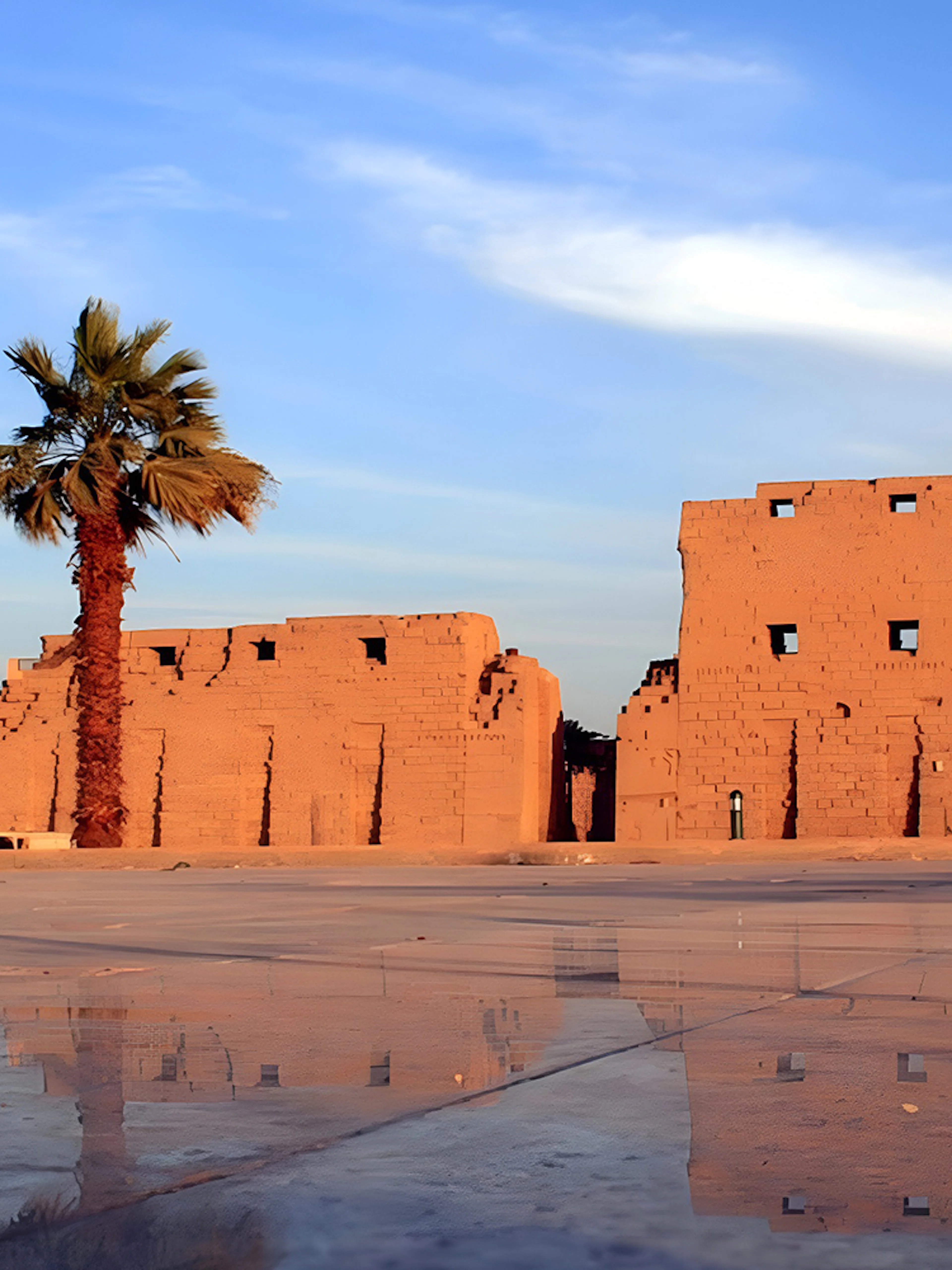 Luxor Temple ruins with palm tree and reflection on wet ground, Egypt.