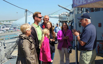 Group listening to a guide on a ship deck during a museum tour with scavenger hunt access.