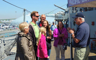 Group listening to a guide on a ship deck during a museum tour with scavenger hunt access.