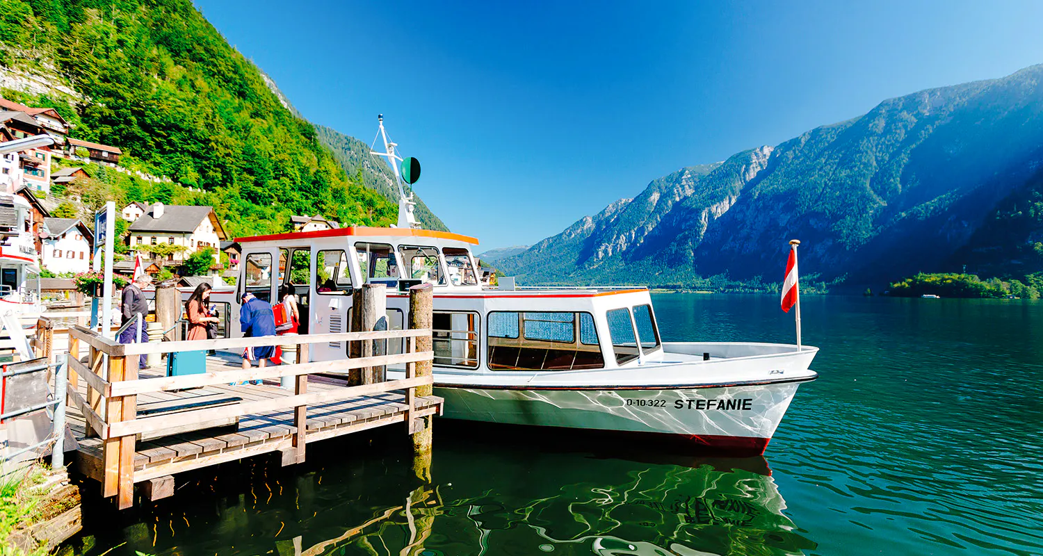 Boat docked at Hallstatt lake with passengers boarding, surrounded by mountains and village houses.