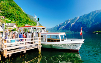 Boat docked at Hallstatt lake with passengers boarding, surrounded by mountains and village houses.