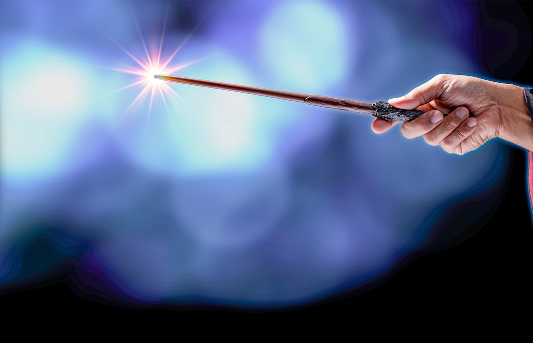 Hand holding a wand with a glowing tip against a blurred blue background.