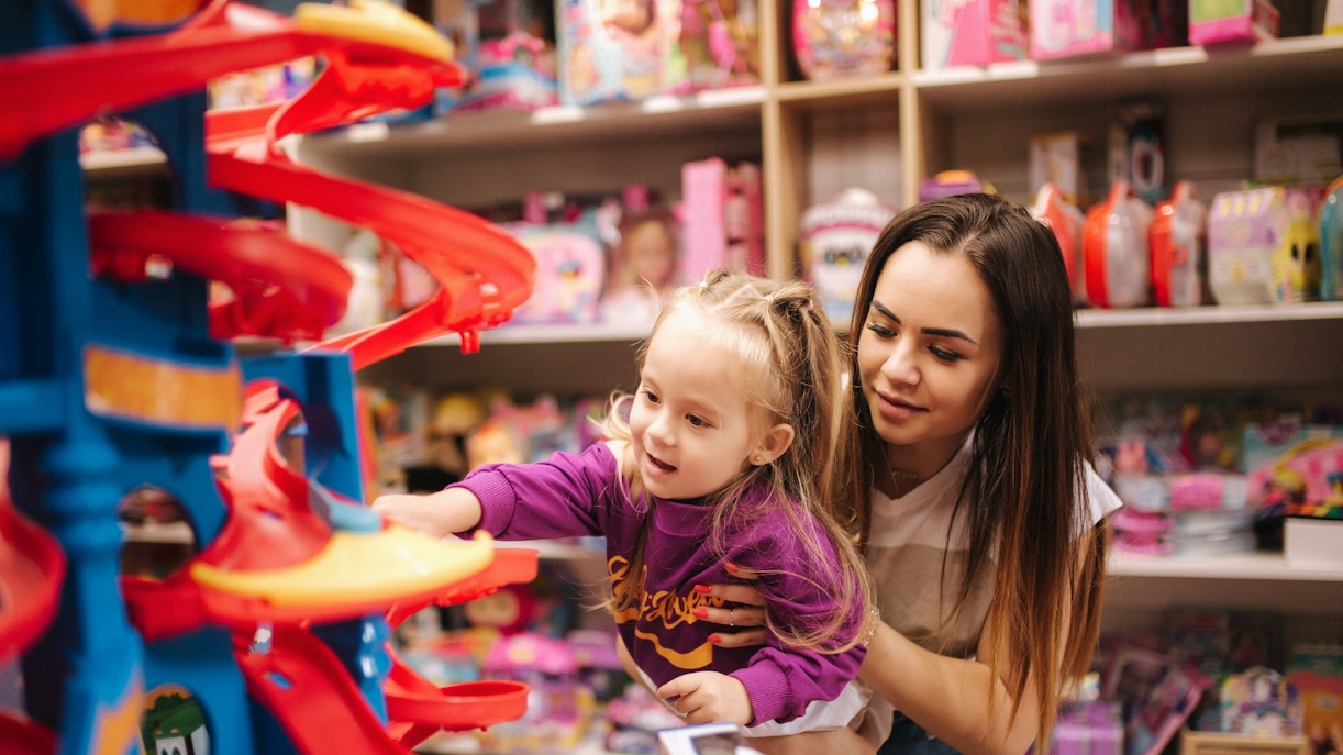 Mother and daughter shopping for toys in a store aisle, exploring various options.