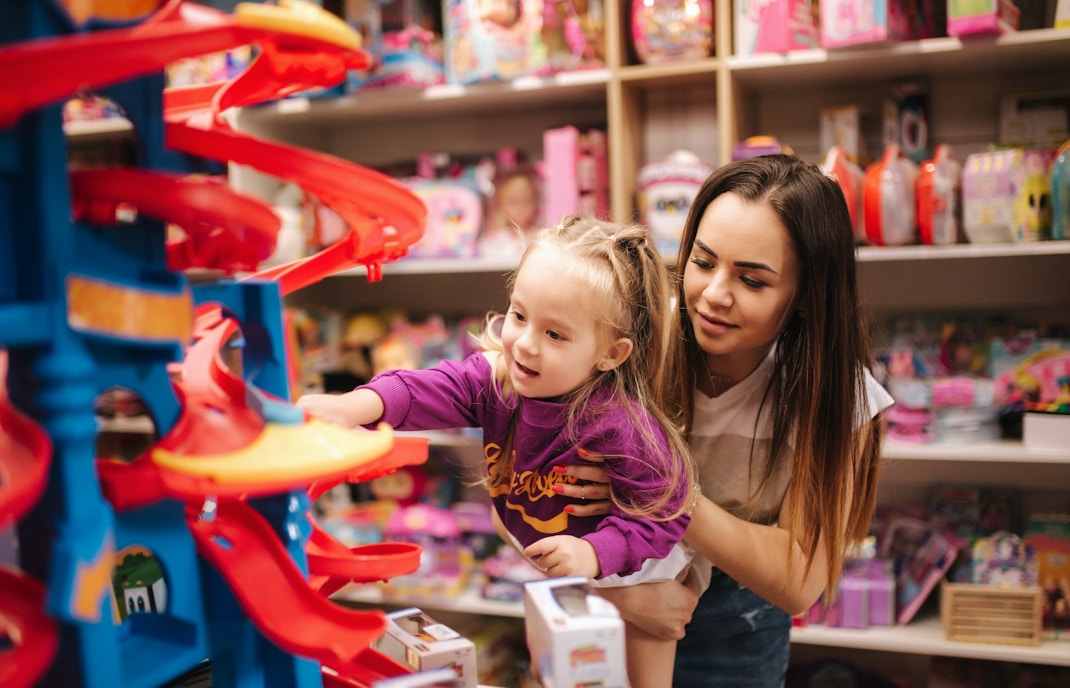 Mother and daughter shopping for toys in a store aisle, exploring various options.