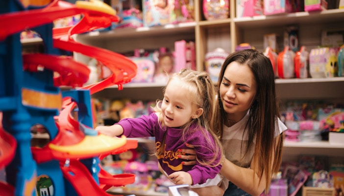 Mother and daughter shopping for toys in a store aisle, exploring various options.