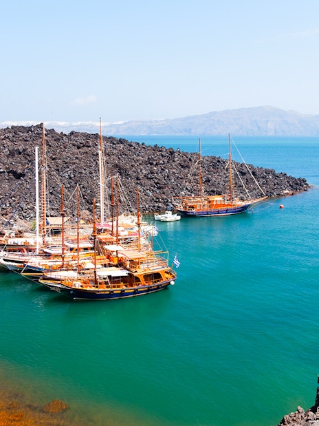 Boats anchored near volcanic rocks at Santorini Volcano Hot Springs, Thirassia.