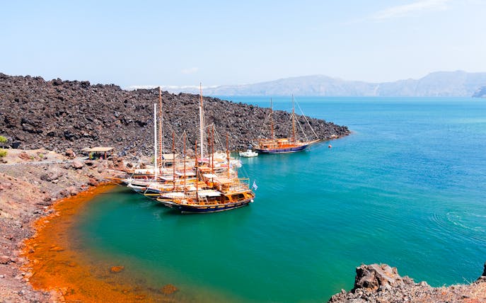 Boats anchored near volcanic rocks at Santorini Volcano Hot Springs, Thirassia.