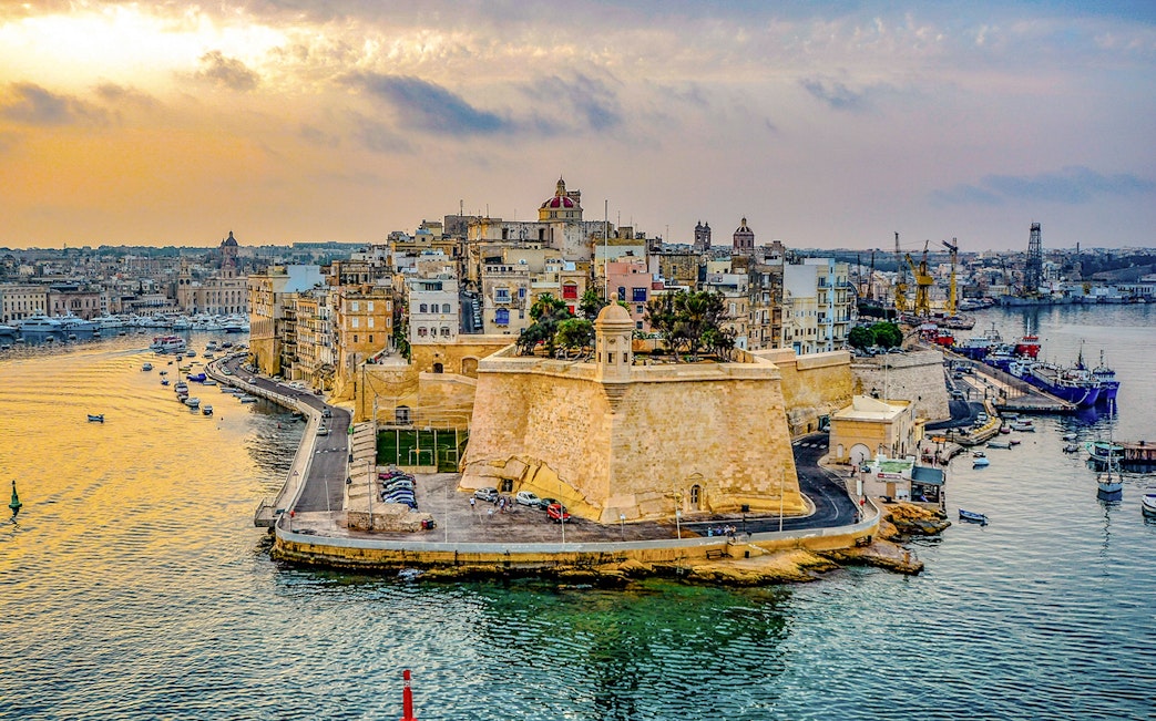 Aerial view of Valletta's historic fortifications and harbor in Malta at sunset.