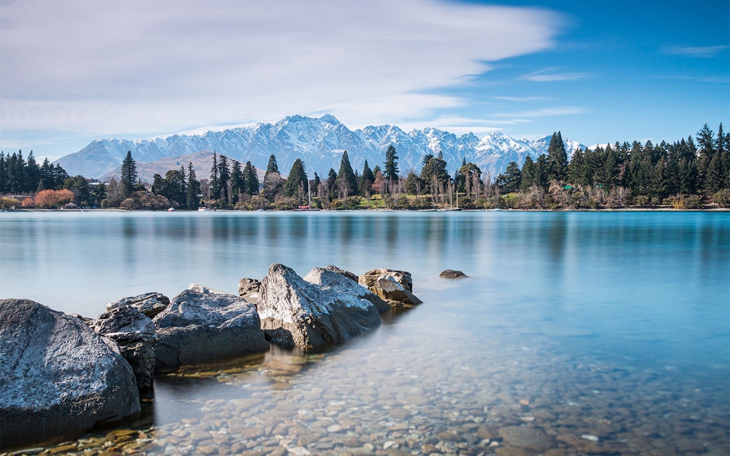 Rocky shoreline of Lake Wakatipu with mountains in Queenstown, New Zealand.