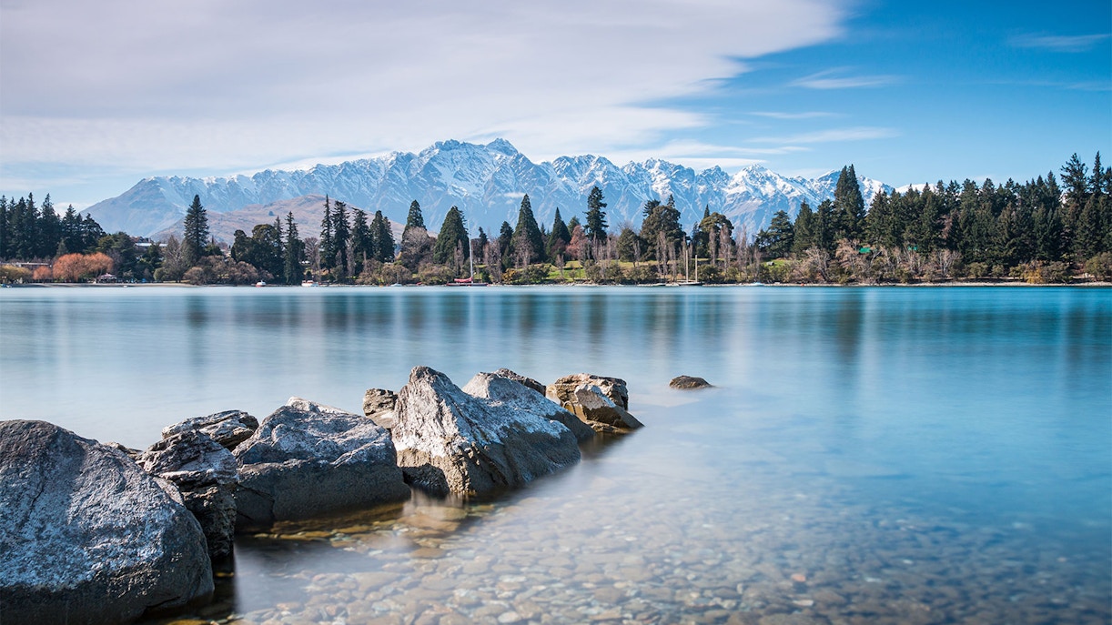 Rocky shoreline of Lake Wakatipu with mountains in Queenstown, New Zealand.