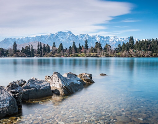 Rocky shoreline of Lake Wakatipu with mountains in Queenstown, New Zealand.