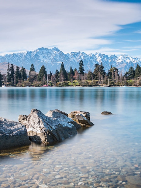 Rocky shoreline of Lake Wakatipu with mountains in Queenstown, New Zealand.