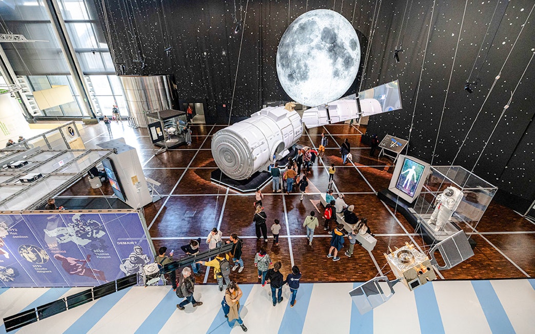 Visitors exploring space exhibit at Science & Industry Museum, Paris, featuring spacecraft and moon display.