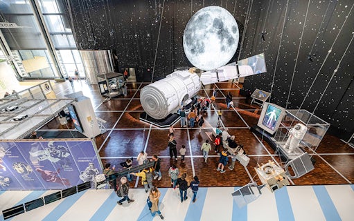 Visitors exploring space exhibit at Science & Industry Museum, Paris, featuring spacecraft and moon display.