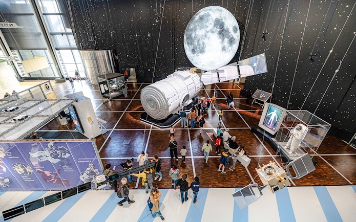 Visitors exploring space exhibit at Science & Industry Museum, Paris, featuring spacecraft and moon display.
