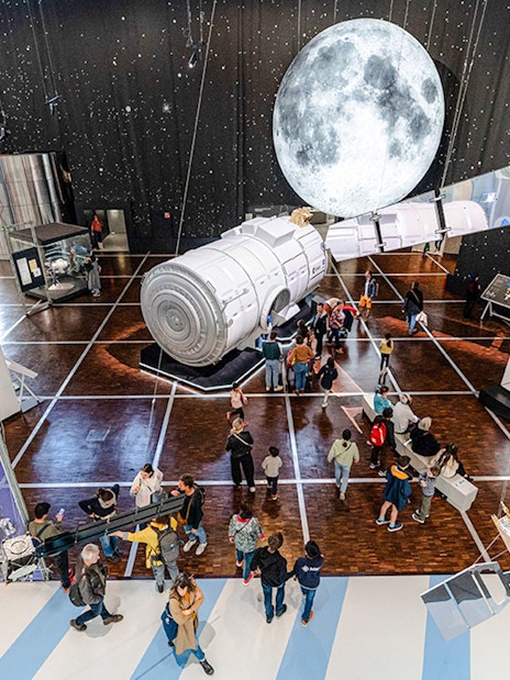 Visitors exploring space exhibit at Science & Industry Museum, Paris, featuring spacecraft and moon display.