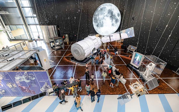 Visitors exploring space exhibit at Science & Industry Museum, Paris, featuring spacecraft and moon display.