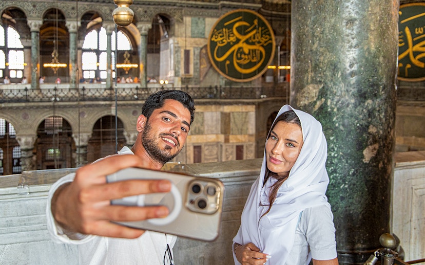 Visitors taking a selfie inside Hagia Sophia, Istanbul, with ornate interior details.