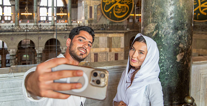 Visitors taking a selfie inside Hagia Sophia, Istanbul, with ornate interior details.