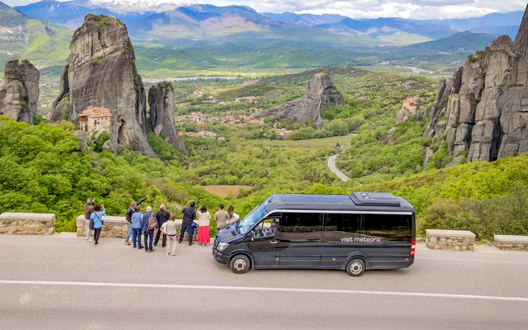 Tour group viewing Meteora rock formations and monastery during guided hiking transfer.