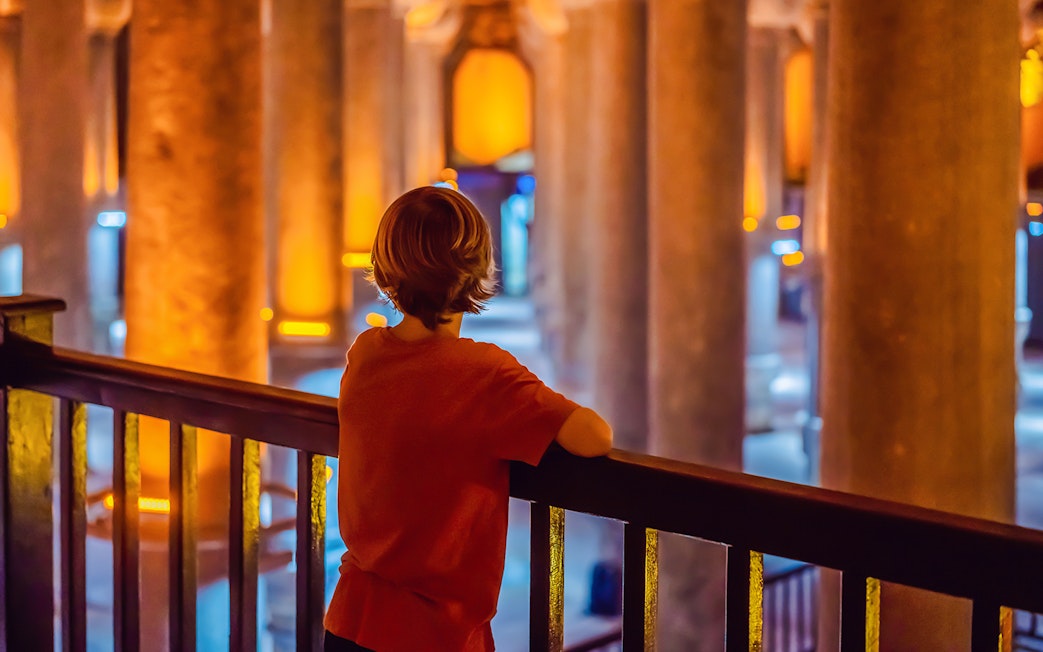 Boy tourist admiring illuminated columns in Istanbul cistern.