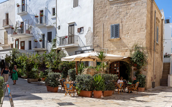 Outdoor café in the old town of Polignano a Mare, Apulia, with people dining under umbrellas.