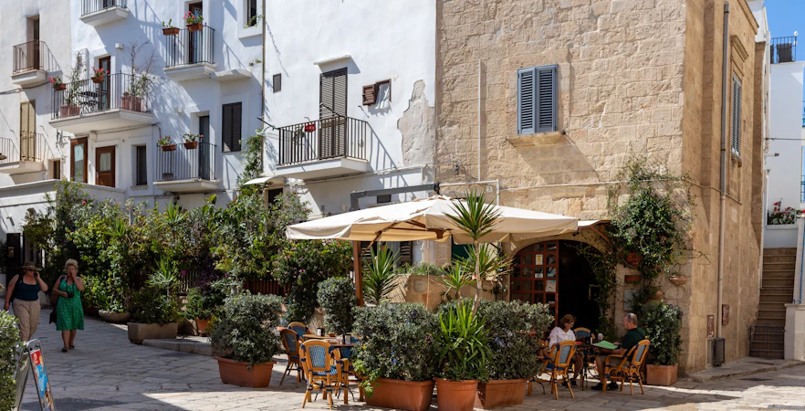 Outdoor café in the old town of Polignano a Mare, Apulia, with people dining under umbrellas.